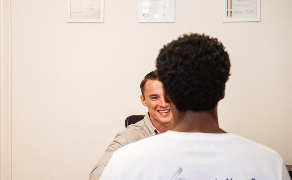 A man sitting at a desk, smiling and talking to a patient.