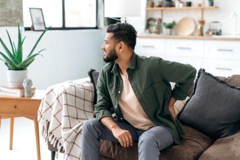 arabian-indian-man-dressed-casual-wear-sitting-sofa-living-room-experiencing-acute-pain-back